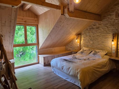Chambre rustique en loft à La R'Mise de Surcey avec poutres apparentes, murs de pierre, lit double et grande fenêtre avec vue