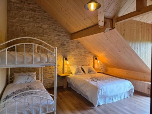Chambre mansardée cosy à La R'Mise de Surcey avec lits superposés, murs en pierre apparente, poutres en bois et vue sur le jardin