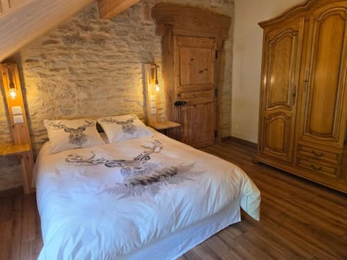 Chambre rustique à La R'Mise de Surcey avec murs en pierre, lit en bois, literie élégante et armoire en bois.