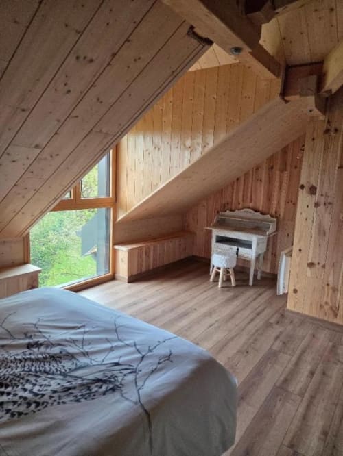 Chambre douillette sous les combles de La R'Mise de Surcey avec poutres apparentes, lit, bureau et vue sur le jardin par grande fenêtre