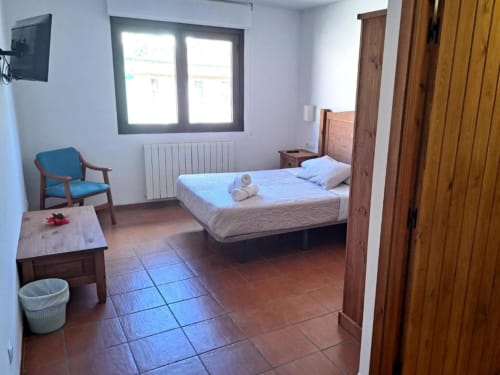 Habitación luminosa con cama doble, TV, sillón y mobiliario de madera en Hostal Monterde de Albarracín