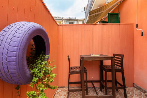 Colorful courtyard at Casa Scola Loano with purple tire planter, wooden bar seating, and orange walls in Loano, Italy
