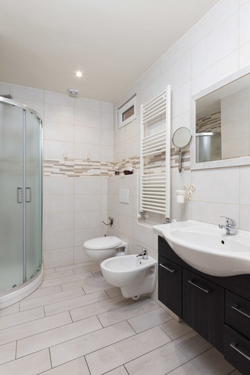 Modern bathroom in Casa Scola Loano with white tiles, shower, toilet, bidet, and dark vanity in Angetto room, Loano, Italy