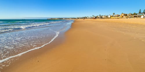 Playa de arena pristina con olas turquesas y casas costeras en Barrosa Home, España