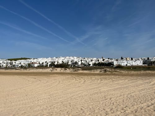 Edificios blancos frente al mar de Barrosa Home con vista a playa de arena y cielo azul despejado