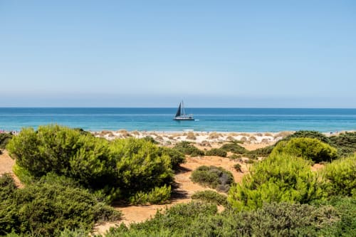 Velero anclado frente a la prístina playa de Barrosa Home, España, con dunas costeras y Mar Mediterráneo