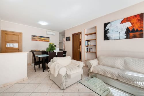 Appartamento Annamaria a Casa Scola Loano, con poltrona beige, letto, tavolo da pranzo, scaffali e quadri.