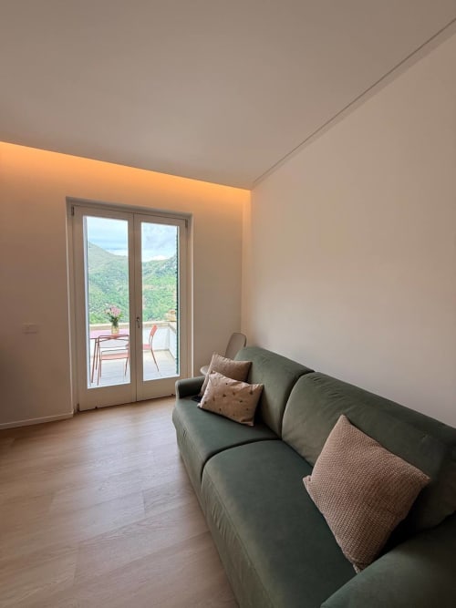 Modern apartment living room at Adagio Ravello with green sofa, wooden floors, and mountain views through glass doors