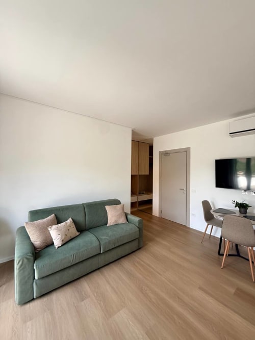 Modern living room at Adagio Ravello apartment with green sofa, wooden flooring, TV, and mountain views in Ravello, Italy