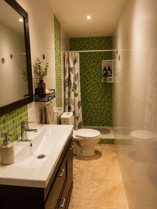 Baño moderno en el apartamento Estada Rural con ducha de azulejos verdes, lavabo blanco, inodoro e iluminación cálida