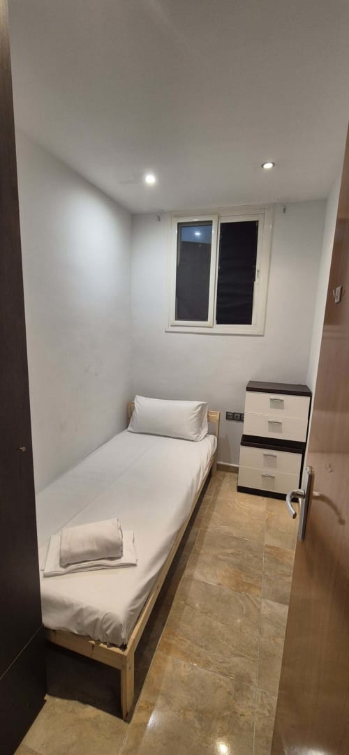 Dormitorio compacto con cama individual, ropa de cama blanca, cajonera y ventana con vistas a la ciudad en el Estada Rural