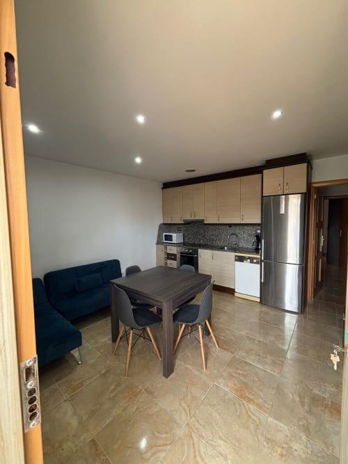 Cocina abierta y comedor en el Apt. Dàlies con mesa oscura, sofá azul marino, electrodomésticos de acero inoxidable y techo moderno