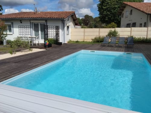Bright turquoise swimming pool with dark wooden deck terrace at La Pause Landaise cottage in Magescq, France