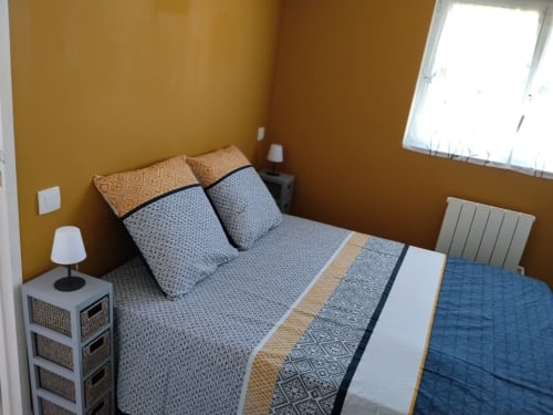 Cozy bedroom at La Pause Landaise cottage with mustard walls, layered bedding, and window with pool view in Magescq