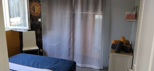Bright bedroom with blue quilted bed, white sheer curtains, and wooden hangers at La Pause Landaise cottage in Magescq
