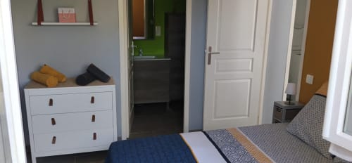 Bright bedroom at La Pause Landaise cottage with bed, white dresser, open bathroom and kitchen entrance in Magescq, France