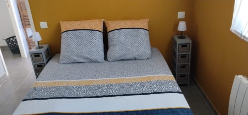 Cozy bedroom in Le Petit Baigneur cottage at La Pause Landaise with mustard walls, blue patterned bedding, and twin