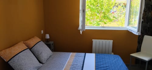 Cozy bedroom at La Pause Landaise cottage in Magescq with blue bedding, mustard walls, and pool garden view