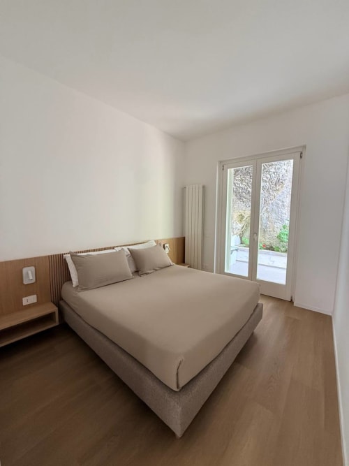 Modern bedroom with beige bedding at Adagio Ravello villa in Ravello, featuring wooden headboard and terrace doors