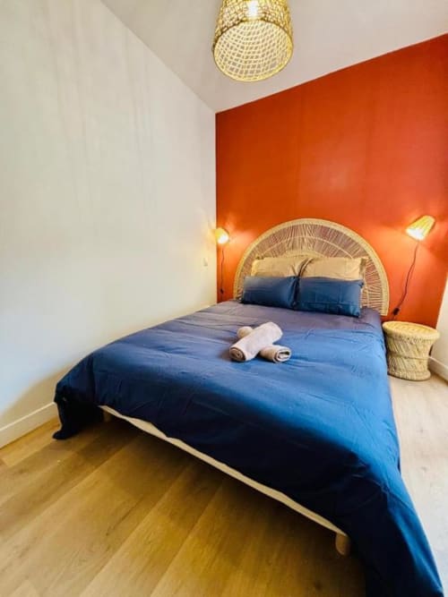 Chambre moderne aux Logis d'Emma : literie bleue, tête de lit tressée, mur d'accent orangé et mobilier en osier