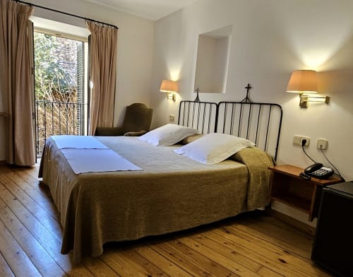 Bright double bedroom at Hotel de la Font Perelada with garden views, wrought iron bed, wooden floors, and modern amenities