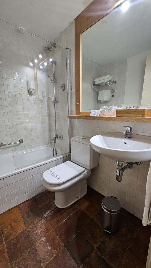 Modern bathroom with white tile walls, glass shower enclosure, circular sink, and wooden mirror frame at Hotel de la Font