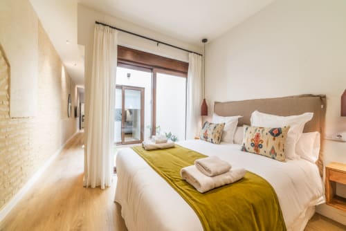 Dormitorio moderno en Los Patios de Feria de Sevilla con cama doble, colcha chartreuse, ropa blanca y acceso a terraza