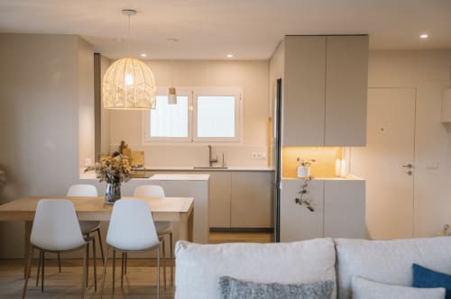 Modern kitchen and dining area in Palafrugell apartment with pendant light, white chairs, and contemporary cabinetry