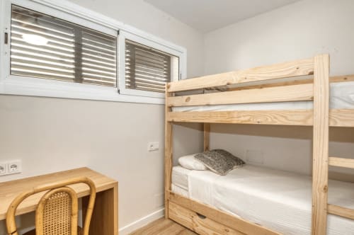 Bright bedroom with wooden bunk beds, desk, and shuttered window at Finques Garcia Enrich apartment in Palafrugell