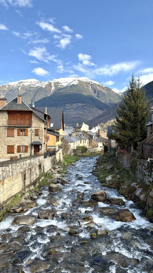 Arroyo de montaña atravesando el pueblo tradicional de piedra en Vielha, Pirineos con picos nevados