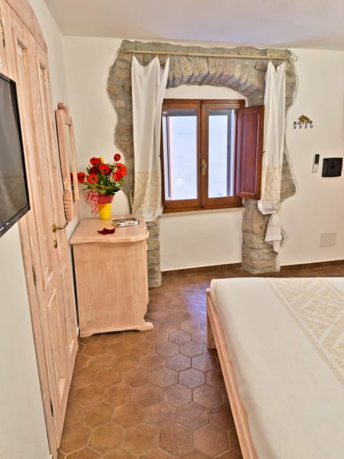 Ampia camera da letto con pavimenti in cotto, porte in legno e finestra luminosa presso Regnos Altos Boutique Rooms a Bosa