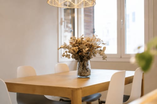 Modern dining room with wooden table, cream chairs, dried flowers, and pendant light in Palafrugell apartment