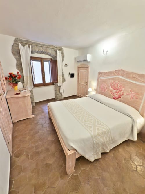 Spaziosa camera matrimoniale a Regnos Altos Boutique Rooms a Bosa con letto in legno, pavimenti in cotto e finestra in pietra