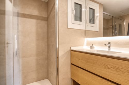Modern bathroom with wooden vanity, white sink, illuminated mirror, beige tile walls, and walk-in shower in Palafrugell