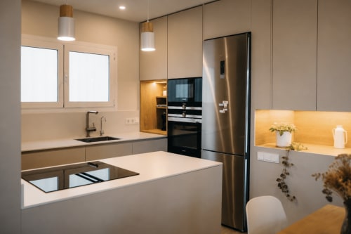 Modern kitchen with white cabinetry, stainless steel appliances, and golden accent lighting in Palafrugell apartment
