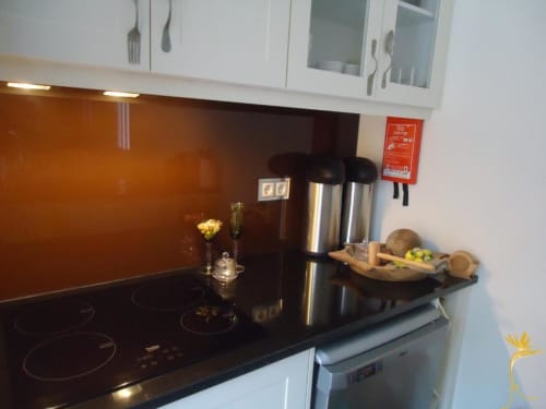 Cozinha moderna com backsplash laranja, fogão preto, eletrodomésticos em aço inoxidável e armários brancos na Casa