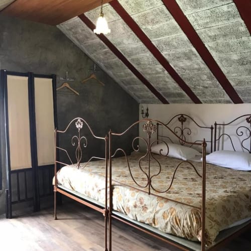 Quarto na mansarda com camas de ferro ornamentadas, vigas aparentes e teto inclinado na villa Casa Estrelícia-Dourada Garcês em São Vicente