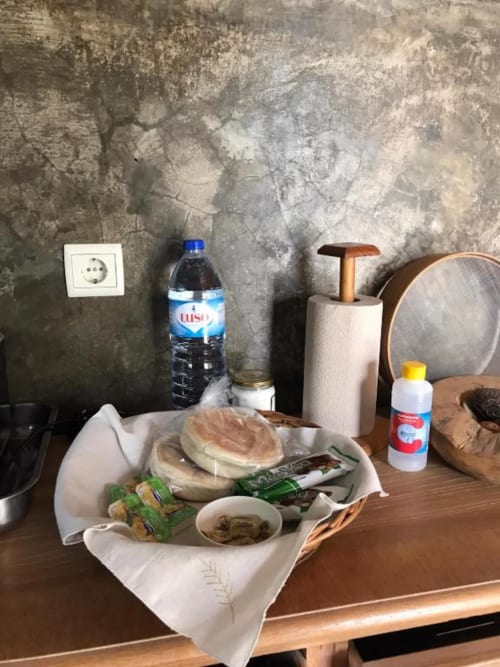 Café da manhã na villa Casa Estrelícia em São Vicente com pão, frutos do mar, vegetais verdes e garrafa de água sobre madeira