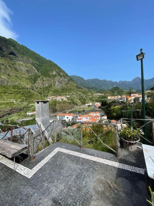 Vista da varanda da aldeia de São Vicente com montanhas, casarões de telhado vermelho e encostas verdejantes desde a Casa