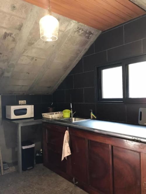 Cozinha moderna em sótão com paredes de azulejo escuro, bancadas de madeira, micro-ondas e grande janela com vista para São Vicente, Portugal