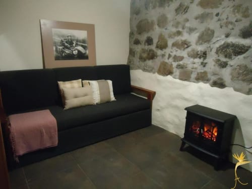 Aconchegante sala de estar de vila em pedra com sofá preto, lareira e roupa de cama branca em A Casa Estrelícia-Dourada Garcês em São