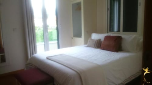 Quarto claro com cama branca, varanda com vista para o oceano e jardim na Casa Estrelícia-Dourada, São Vicente