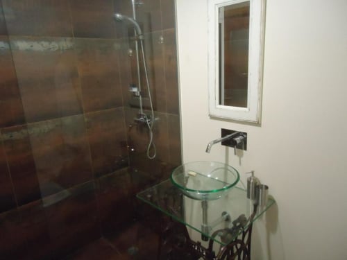 Banheiro moderno com box de vidro, lavatório circular em vidro, torneira de parede e espelho na Casa Estrelícia-Dourada