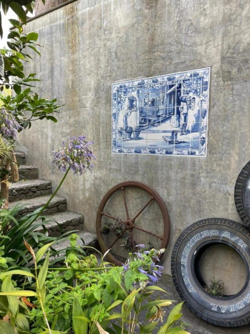 Pátio rústico da Casa Estrelícia-Dourada Garcês em São Vicente com painel de azulejos azuis, roda vintage e flores