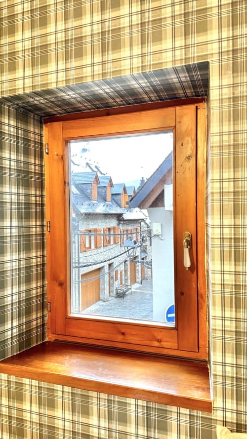 Ventana de madera con vistas a la arquitectura alpina tradicional en un apartamento de montaña en Vielha