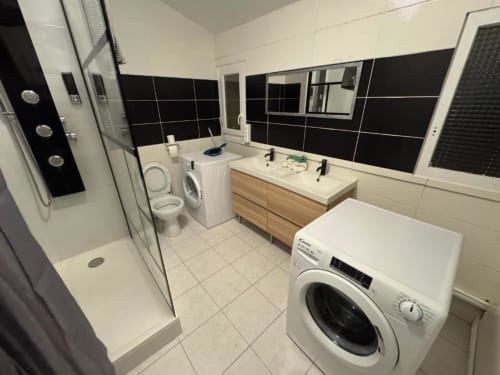 Salle de bain moderne aux murs carrelés noir et blanc, double vasque, lave-linge, toilettes et douche vitrée