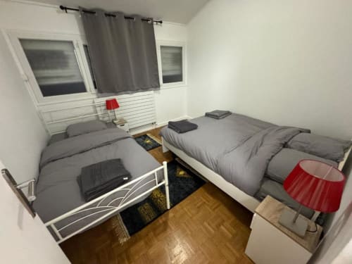 Appartement 2 chambres à Kawichimmo Locations à Louvres avec deux lits simples, literie grise, parquet et accent rouge
