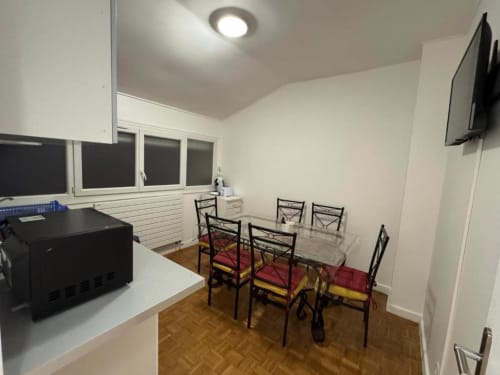 Espace repas moderne dans un appartement Kawichimmo avec table en verre, chaises noires, kitchenette et TV murale