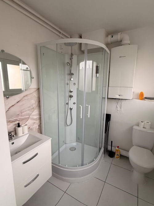 Salle de bains moderne avec douche à l'italienne, vasque blanche, toilettes et accents en marbre à l'appartement Kawichimmo Louvres