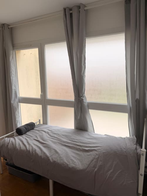 Chambre moderne dans l'appartement Kawichimmo Locations à Louvres, avec lit, grandes fenêtres, rideaux gris et lumière naturelle